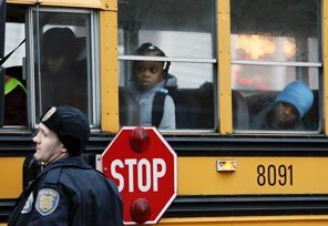 Schoolchildren peer out of a school bus as a police officer explains that their grade school is closed. 