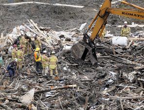 Searchers watch as a machine Wednesday slowly moves debris at the scene of the deadly mudslide. The muck has made rescue work difficult.